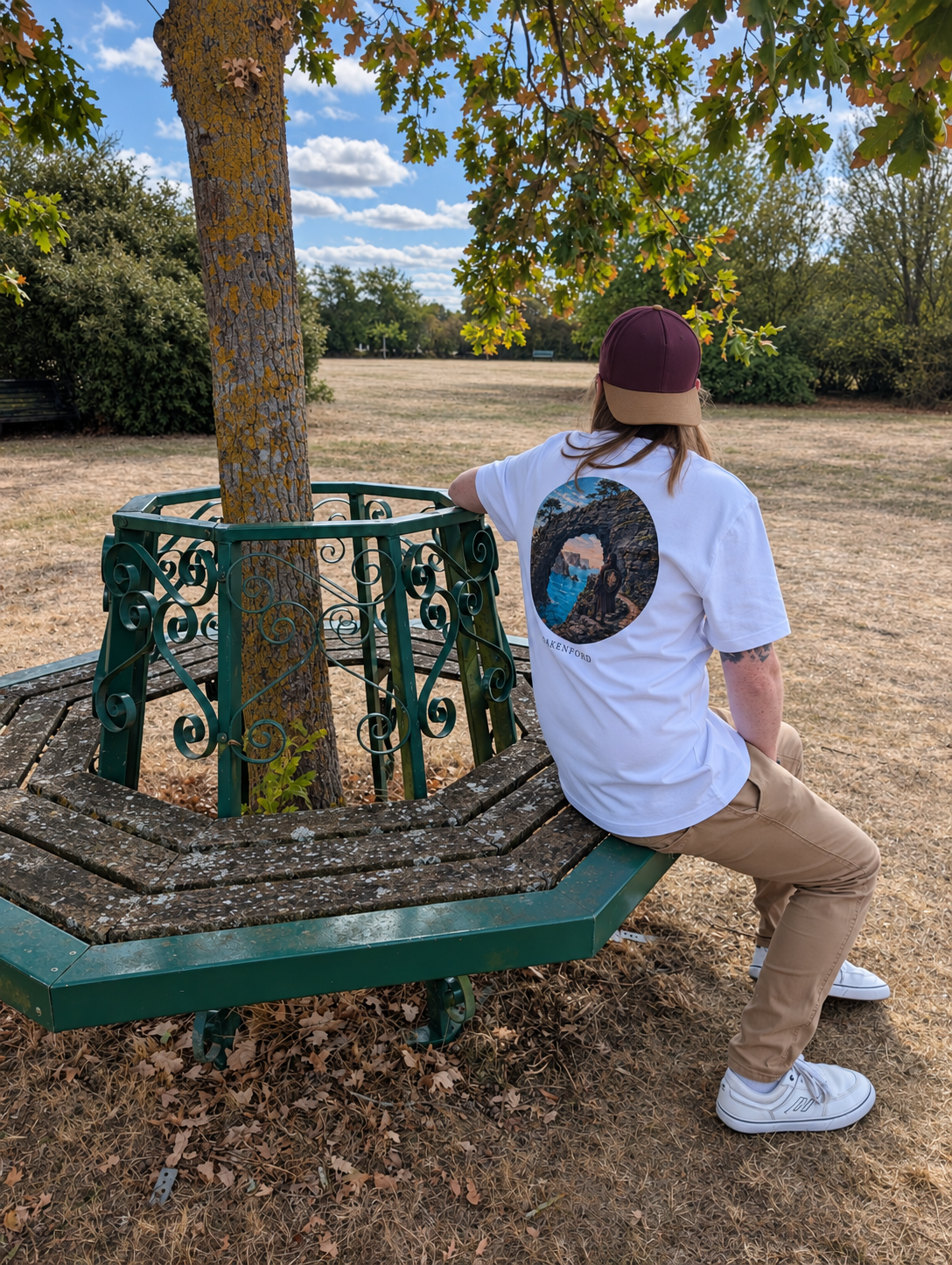 Stone Current white T-shirt worn with tan trousers and white trainers, seated on a bench