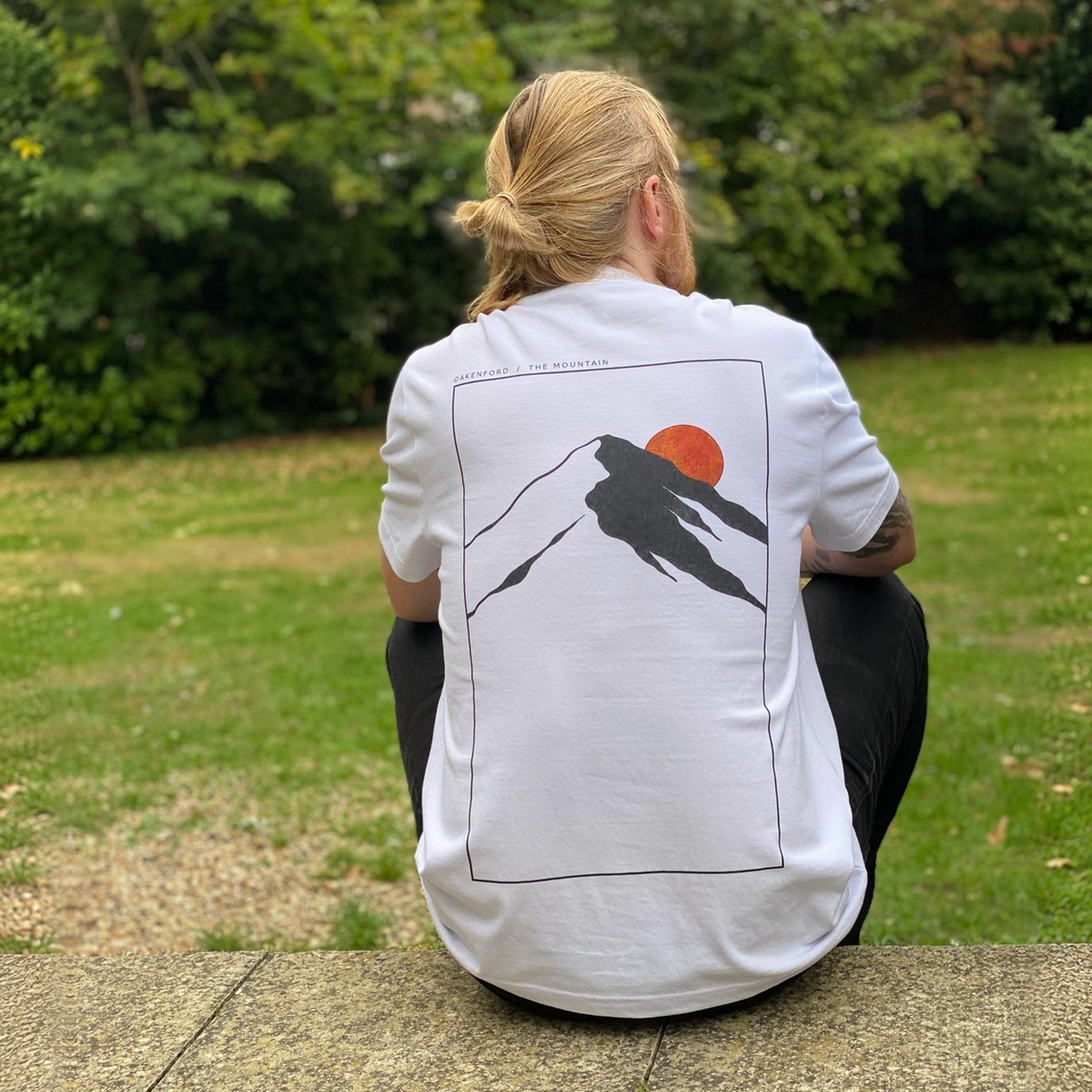 Model seated wearing the white Mountain Oakenford graphic T-shirt