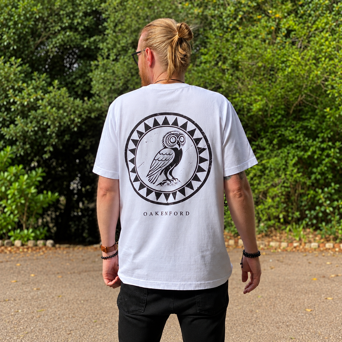 Standing model wearing the white Owl Shield Oakenford graphic T-shirt, back view
