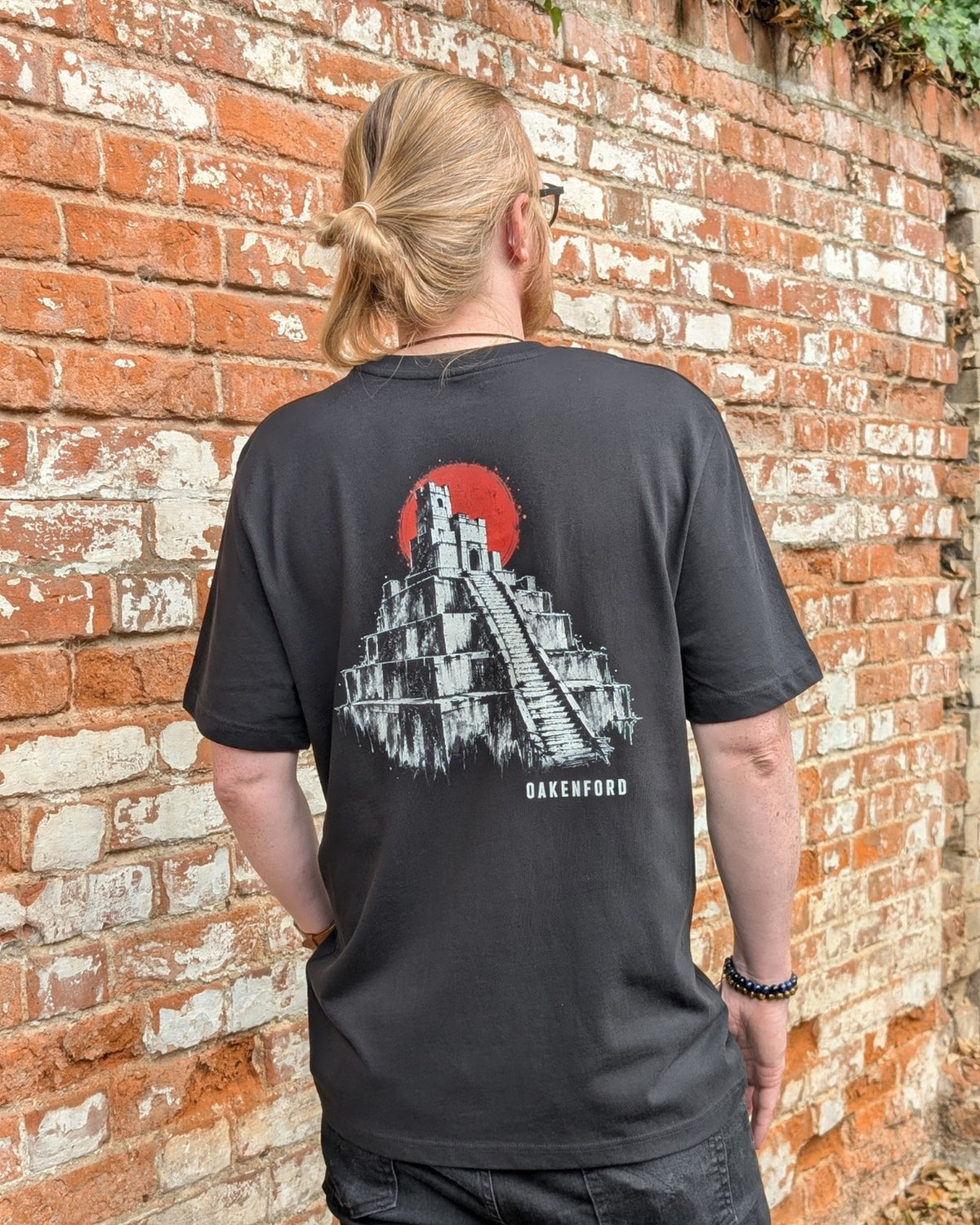 Pyramid black graphic tee worn beside a weathered brick wall