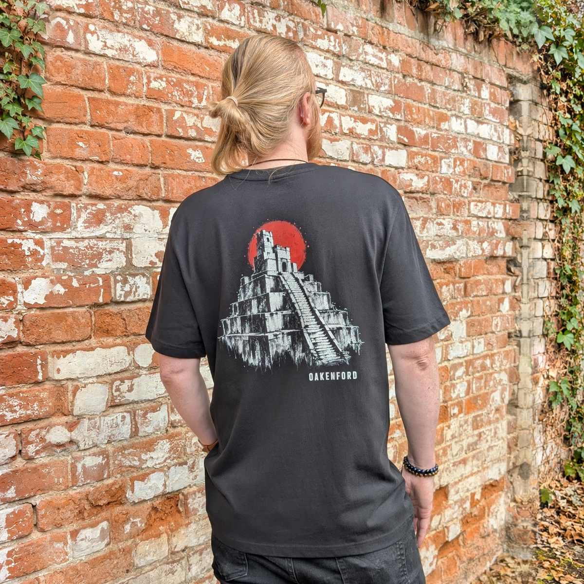 Model wearing the black Pyramid graphic T-shirt beside a brick wall