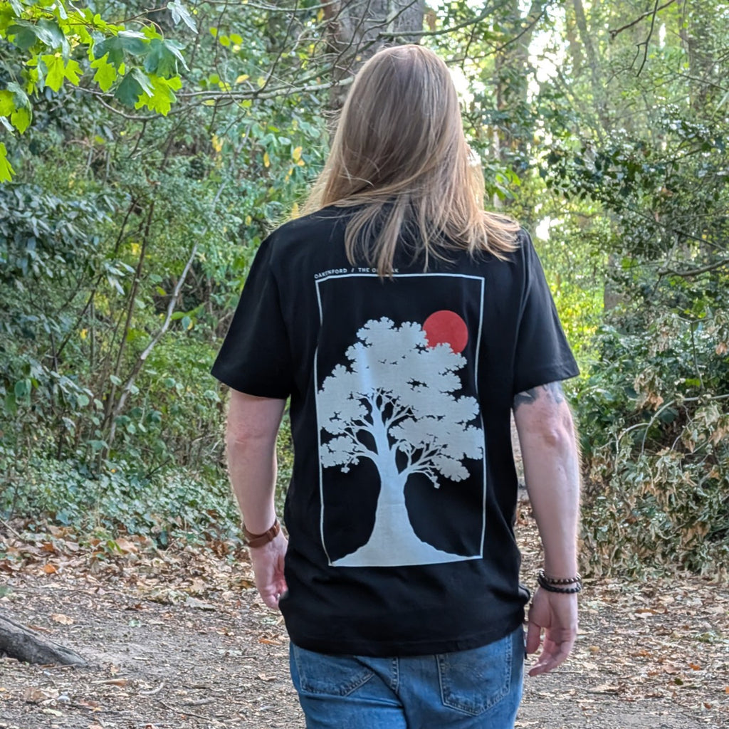 Standing model wearing The Old Oak black T-shirt, back view in woodland