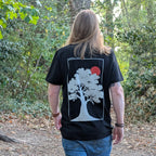 Standing model wearing The Old Oak black T-shirt, back view in woodland