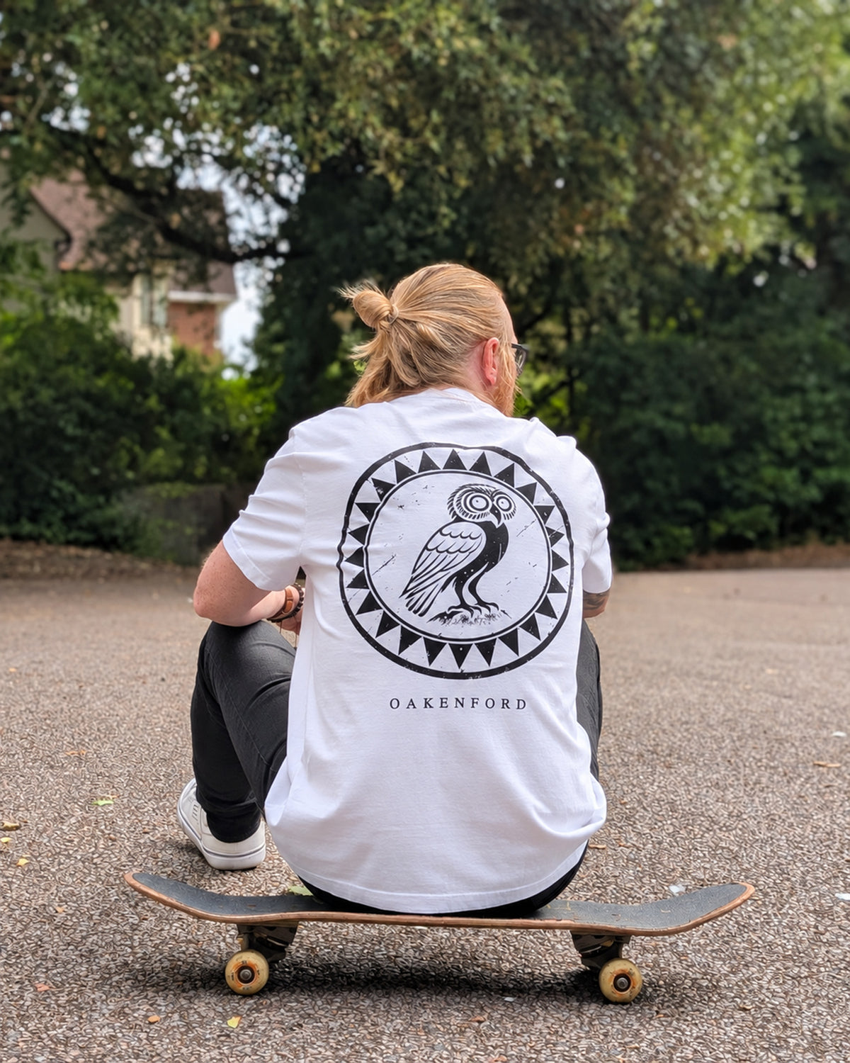 Owl Shield white tee worn seated with a skateboard