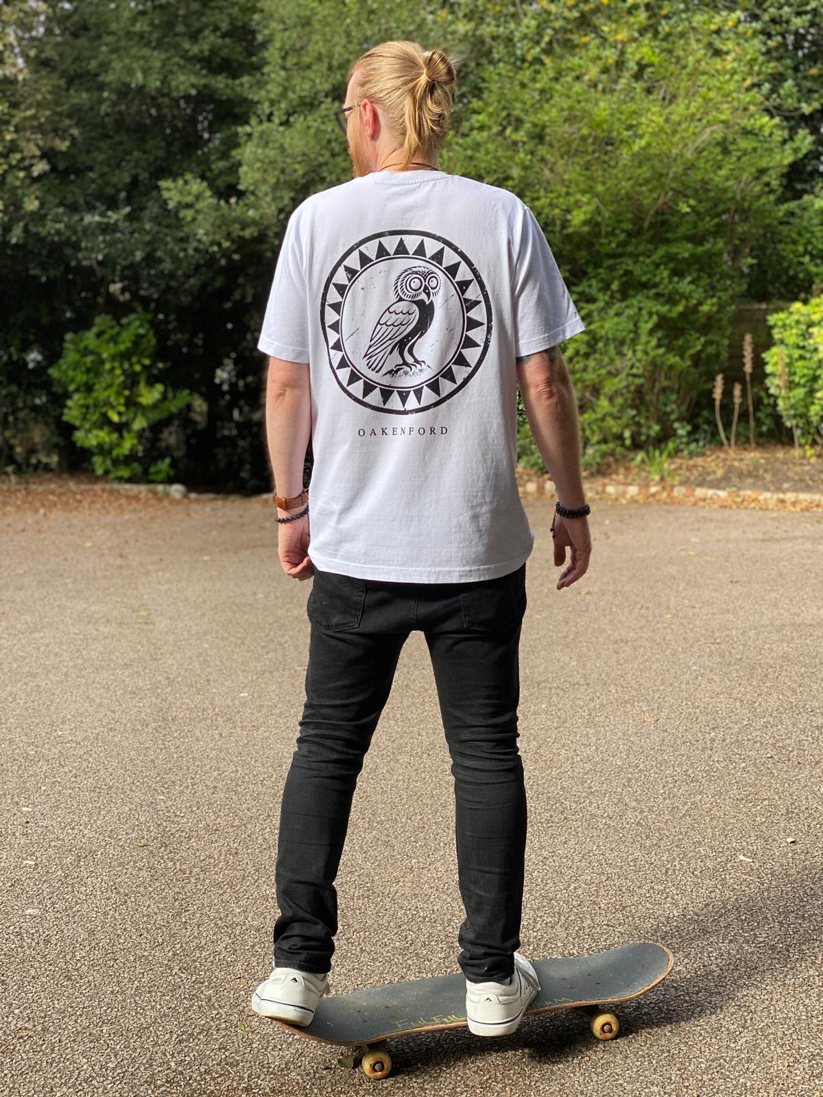 Standing upright on a skateboard wearing the Owl Shield tee, viewed from behind.